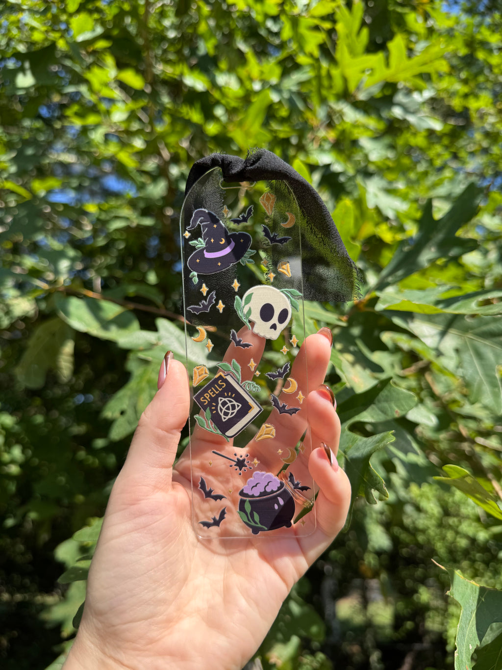 Spells and potions acrylic bookmark with black ribbon held outdoors