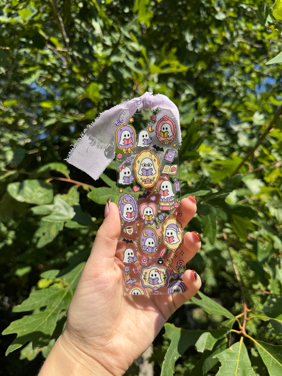 Bookish ghosts acrylic bookmark with lavender ribbon held outdoors