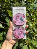 Set of two pink cowboy-boot car coasters in packaging against leafy trees