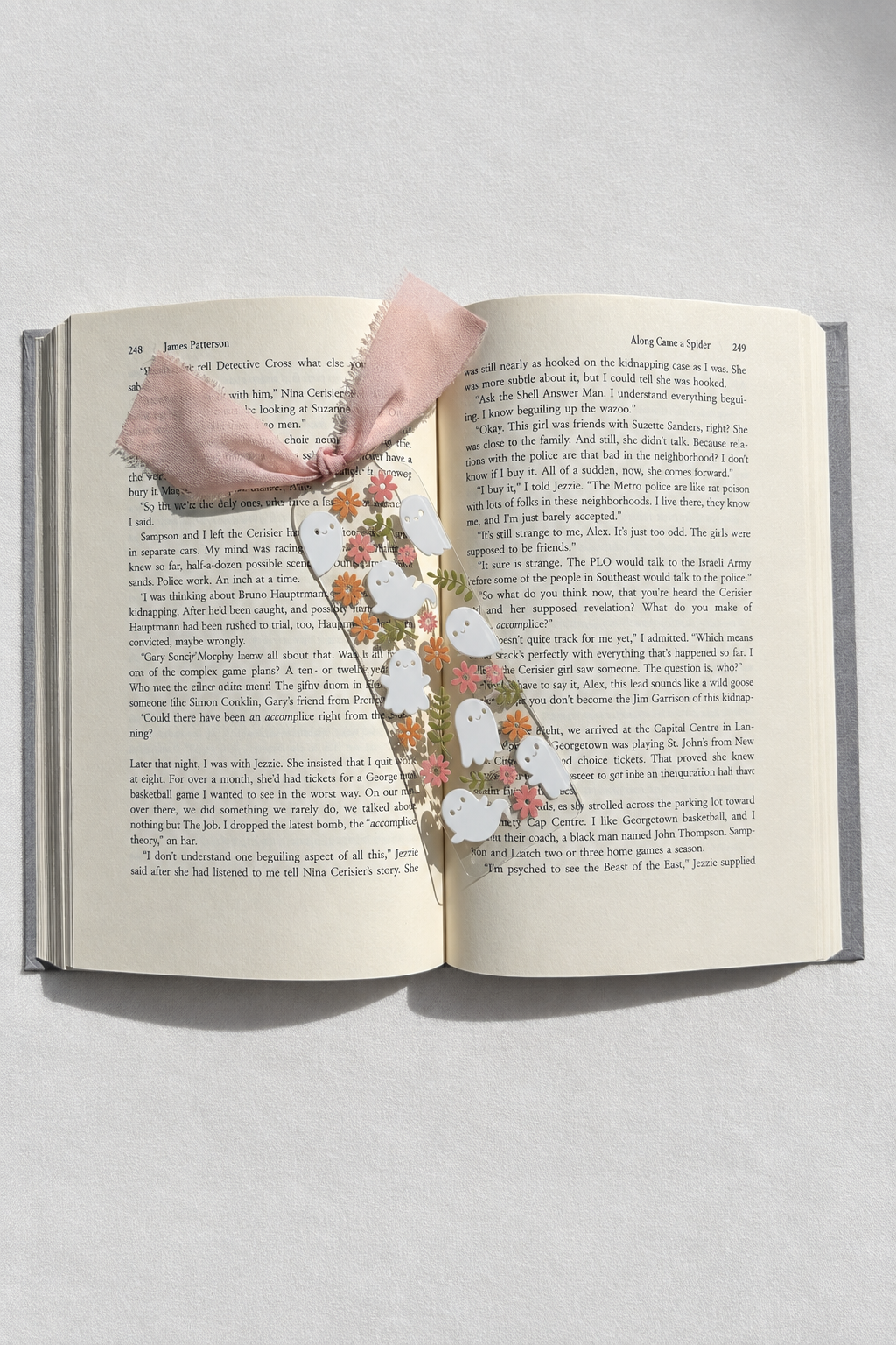 Floral ghosts acrylic bookmark resting on an open book with smooth white fabric backdrop