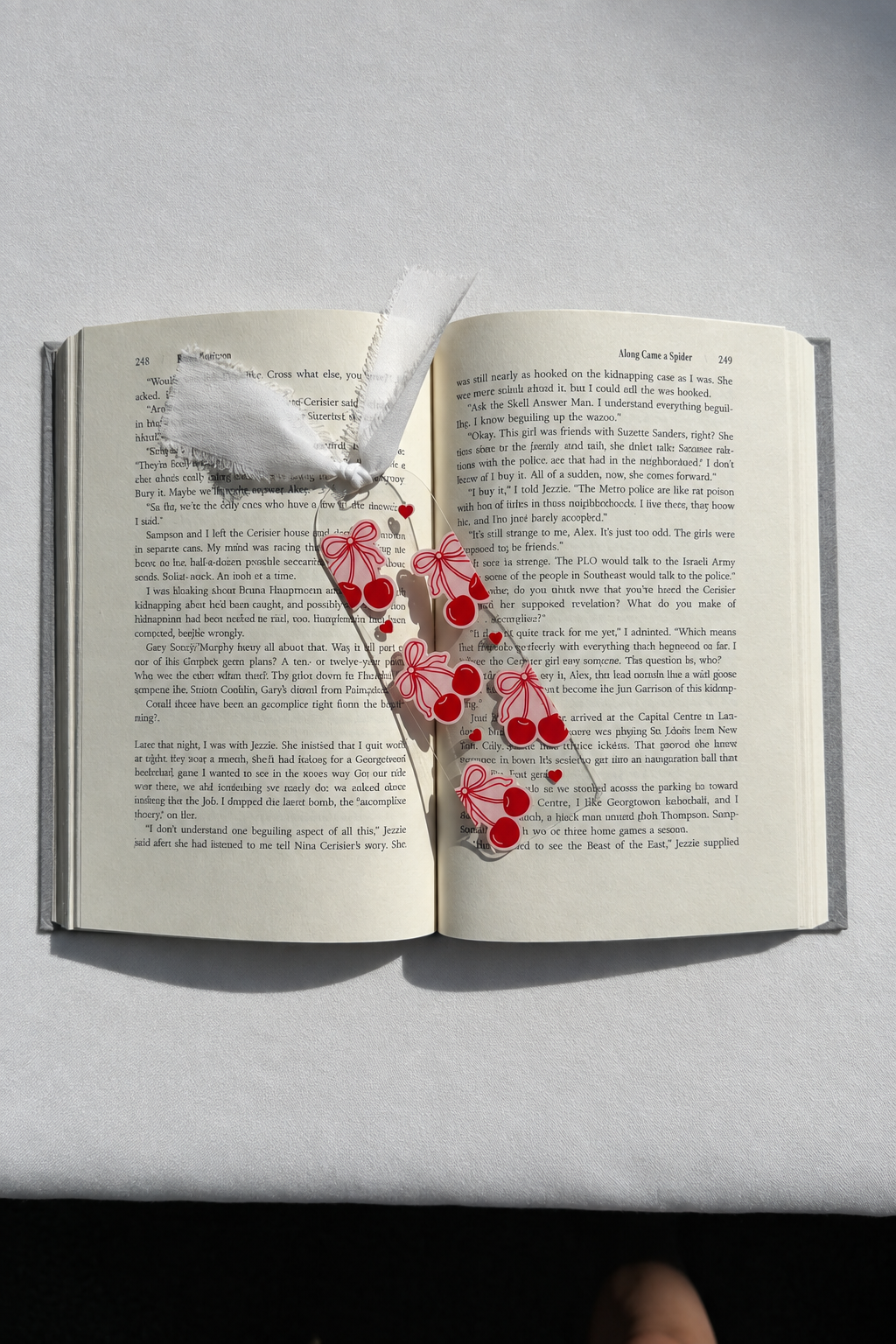 Cherries and bows acrylic bookmark on an open book with smooth white fabric backdrop