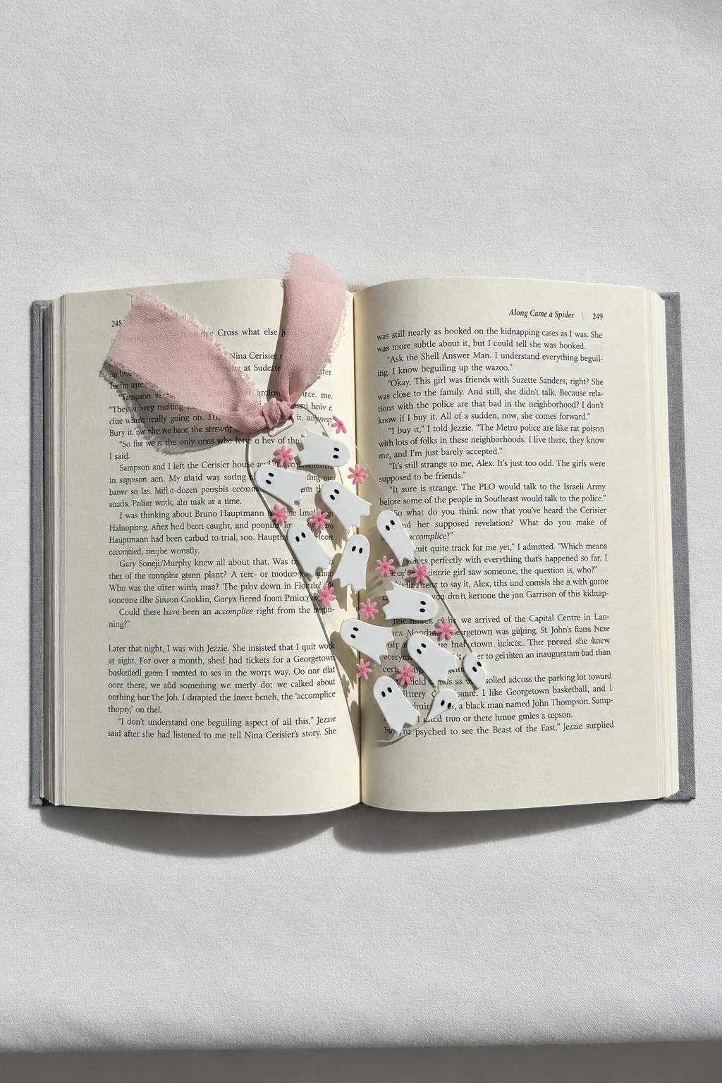 Ghosts and pink flowers acrylic bookmark on an open book with a smooth fabric background